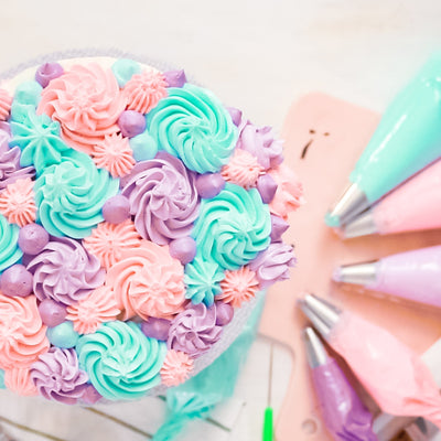 Closed shell piping tips create beautiful icing decorations.  Use a mix of sized tips to create fun cake decorating designs.  This cake is a mix of turquoise, purple, peach, and lavender buttercream icing patterns with piping bags and their tips in the background.
