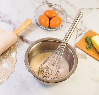 Balloon whisk with ball in a bowl of batter with eggs and butter and a rolling pin.