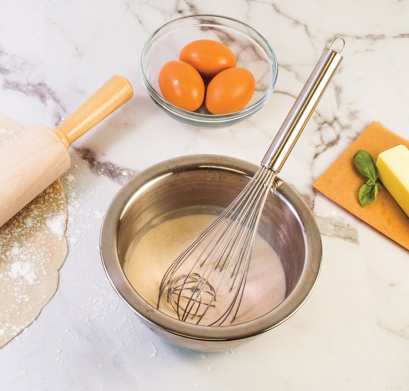 Balloon whisk with ball in a bowl of batter with eggs and butter and a rolling pin.